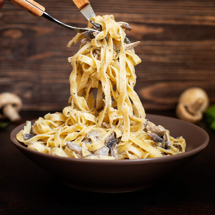 Idea di servizio: fettuccine con funghi e condimento cremoso, sollevate con due posate.